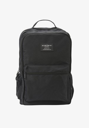 Mochila Koroshi negra fabricada con material duradero, con una forma rectangular, un bolsillo frontal con cremallera y dos bolsillos laterales de malla.