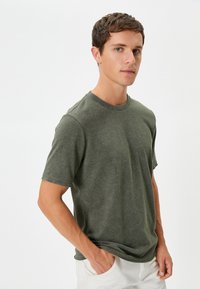 Olivgrön kortärmad t-shirt i texturerat tyg, med en klassisk rund halsringning och en avslappnad passform, kombinerad med ljusa byxor.