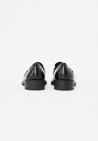 Sorte lærredssko med lav hæl, med en glat tekstur og gyldne hardware-detaljer. Designet med afrundede kanter og minimalistisk stil.