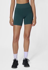 Groene shorts met hoge taille gemaakt van rekbare stof, met een geribbelde textuur. Gecombineerd met zwarte sneakers en witte geribbelde sokken.
