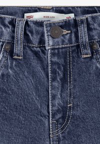 Närbild av blå Levi's vida jeans midja med sydd knapp, bältesloopar och synlig storleksetikett.