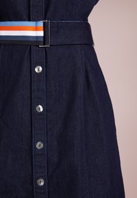 Laivastonsininen farkkumekko, jossa on napillinen etuosa, hopeanväriset napit ja monivärinen raidallinen kangasvyö metallisoljella.