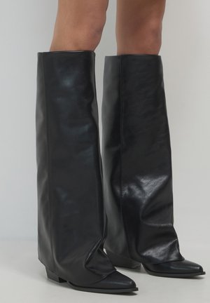 Bottes noires montant jusqu'aux genoux en cuir lisse, présentant un design élégant et décontracté avec des pointes effilées et de petits talons carrés.