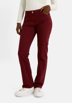 Pantalones slim fit burdeos con un diseño clásico de cinco bolsillos, cierre de botón y detalles de costura sutiles, combinados con zapatillas blancas.