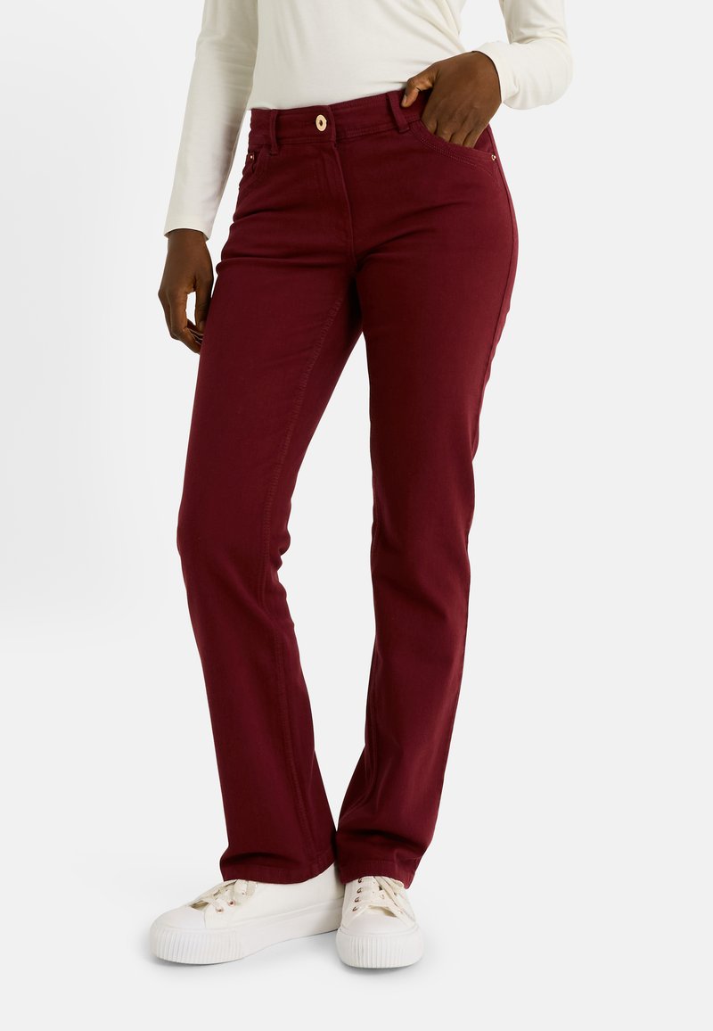 Pantalons bordeaux slim-fit avec une coupe cinq poches classique, fermeture à bouton et détails de couture subtile, associés à des baskets blanches.
