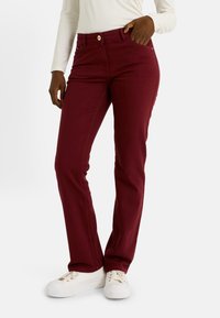 Pantalones slim fit burdeos con un diseño cl�ásico de cinco bolsillos, cierre de botón y detalles de costura sutiles, combinados con zapatillas blancas.