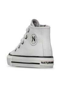 Białe sneakersy za kostkę wykonane z gładkiej skóry; mają czarną gumową podeszwę i akcenty, okrągłą łatkę z logo z boku oraz sznurowany fason.