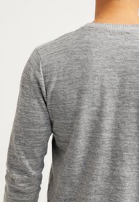 Pull en maille gris avec col rond et manches longues, présentant une texture subtile et une silhouette ajustée. Aucun logo ou motif visible.