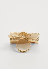 Gold-tone hair clip featuring a textured wave design and a circular loop detail at the base, shiny surface and smooth finish.