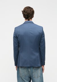 Μπλε σακάκι με λεία υφή, slim fit, με ντεντελέ και δύο κουμπιά, συνδυασμένο με ανοιχτό μπλε τζιν παντελόνι.