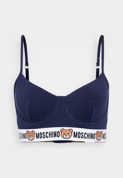 Μπραλέτα από βαμβάκι σε ναυτικό μπλε χρώμα με καλυμμένα cups, λεπτές ρυθμιζόμενες τιράντες και λευκή ζώνη που φέρει γραφικό αρκούδας και κείμενο "MOSCHINO".