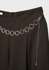 Pantalon noir taille haute avec ceinture chaîne argentée composée de grands maillons circulaires et une fine chaîne pendante avec un fermoir.