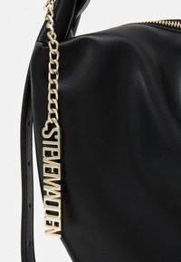 Zwarte leren handtas met een gestructureerd oppervlak, voorzien van een gouden kettinghandvat en logo-accent. Ritsluiting aan de bovenkant.