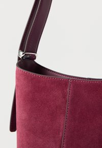 Χειροποίητη τσάντα από βελούδινο σουέντ σε βουργουνδί απόχρωση με λείo δερμάτινο λουράκι, διακοσμημένη με τακτοποιημένο ράψιμο και μεταλλικά εξαρτήματα στο σημείο σύνδεσης.
