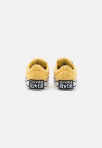 Baskets Converse All Star jaunes avec une silhouette basse, semelles en caoutchouc noir et un logo étoilé blanc à l'arrière. Texture lisse, sans motifs visibles.