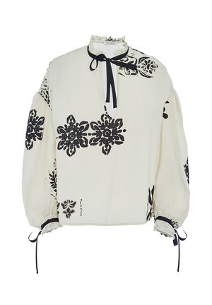 Blusa bianca con motivi floreali neri, colletto arricciato e lacci al collo e alle maniche. Presenta maniche a palloncino e una vestibilità comoda.