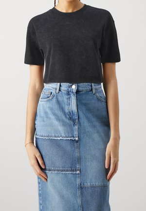 T-shirt nera accorciata con scollatura rotonda abbinata a una gonna di jeans blu con pannelli in patchwork e orli sfilacciati.