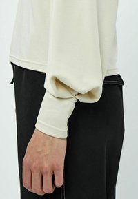 Maglietta a maniche lunghe, di colore crema, con una vestibilità comoda, caratterizzata da polsini a costine e una texture liscia, abbinata a pantaloni neri con vestibilità dritta.