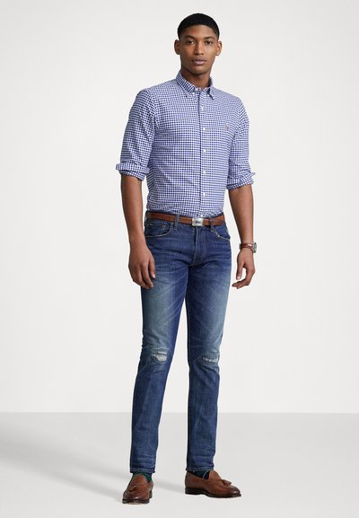 Blue and white checkered button-up shirt, rolled sleeves; fitted dark jeans with distressed details; brown leather belt; brown shoes.