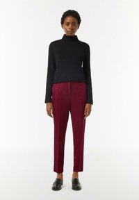 Czarny sweter z golfem, bordowe dopasowane spodnie z kantem i czarne mokasyny. Prosty design, gładka tekstura i dopasowany krój.