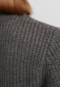 Maglione grigio lavorato a maglia con una trama a costine. Il tessuto appare spesso e accogliente, evidenziando il motivo delle cuciture e il design senza cuciture.