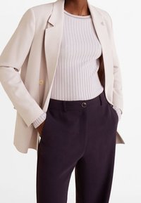 Blazer beige clair sur un top lilas à côtes, associé à un pantalon sur mesure violet foncé. Le tissu semble lisse avec des éléments de design structurés.