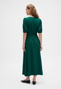 Roheline maksikleit puffy varrukate, elastse vöökoha ja voolava seelikuga. Sile kangapind. Kandmisega mustad tallatud kingad.