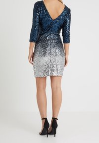Paljettklänning med V-rygg, som har en gradient från marinblått till silver. Trekvartsärmar och en figurnära siluett. Svarta högklackade skor.