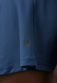 Camisola desportiva azul com uma textura suave, mangas curtas e um detalhe de logotipo preto próximo à bainha. Tecido leve e respirável.
