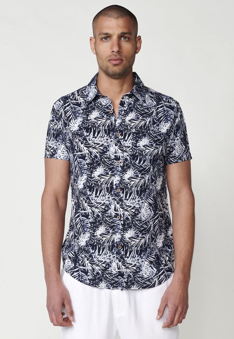 Kratke rokave srajca v temno modri barvi z belim botaničnim vzorcem. Ima ovratnik in rjave gumbe ter je izdelana iz mehkega materiala.