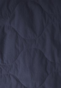 Dunkelblaue Stoff mit einem dezenten gewellten Stichmuster, das geschwungene Linien über die Oberfläche zieht.