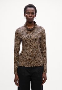 Leoparda raksta garās piedurknes tops ar kraukšķīgu kakla izgriezumu, kas izgatavots no gludas tekstūras brūnā un melnā krāsā. Valkāts ar melnajām biksēm.