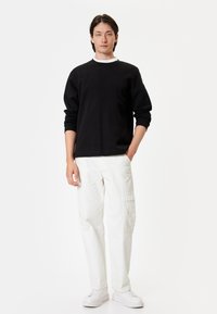 Czarna bluza z białym kołnierzykiem, połączona z białymi spodniami cargo z bocznymi kieszeniami oraz białymi sneakersami o eleganckim wzornictwie.
