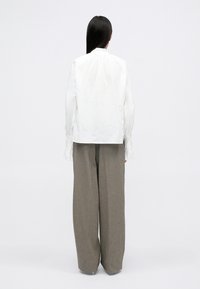 Camicia bianca in cotone con collo alto e dettagli plissettati sul retro, abbinata a pantaloni grigi a gamba larga con una trama testurizzata.