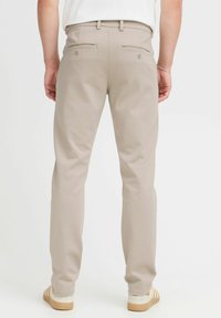 Pantalones de vestir beige con una textura suave, que cuentan con bolsillos traseros y detalles de costura sutiles, combinados con zapatillas ligeras.