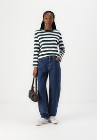 Maglietta a maniche lunghe a righe verde scuro e bianca, abbinata a jeans blu in denim a vita alta, scarpe da ginnastica bianche e una borsa a tracolla marrone.