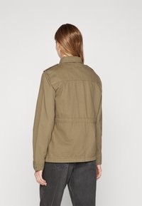 Olive green cotton jacket with a collared neckline, shoulder epaulets, and a cinched waist. Features long sleeves and buttoned cuffs.