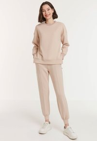 Licht beige sweatshirt en bijpassende taps toelopende broek, met ribbelafwerking, zijstreepjes en zachte stof. Gecombineerd met witte sneakers.