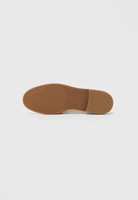 Brun gummisål til sko med tekstureret overflade og rundet tå. Har præget "Michael Kors"-logo og formet design.