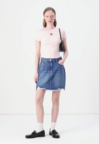 Light pink fitted t-shirt with a small logo, paired with a blue denim skirt featuring frayed hem. Black loafers and white socks complete the look.