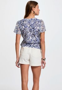 Bloemengeprinte blouse met korte mouwen in blauw en wit, gemaakt van lichte stof, gecombineerd met witte shorts, met een relaxte pasvorm en details op de achterkant.