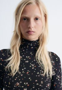 Black floral turtleneck top made of stretch fabric, featuring small multicolored flowers in a scattered pattern across the surface.