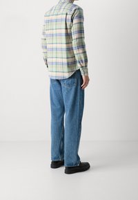 Koszula w kratę z długim rękawem w kolorach zielonym, niebieskim, żółtym i różowym; bawełniana tkanina. Połączona z luźnymi niebieskimi dżinsami i czarnymi butami.