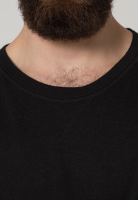 Svart crewneck-tröja med en mjuk textur, som visar en enkel design och subtila stygn detaljer vid halsringningen och axeln.