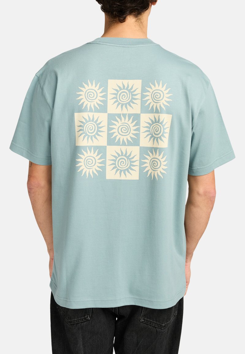 Hellblaues Baumwoll-T-Shirt mit einem großen cremefarbenen Sonnengrafikmuster auf der Rückseite, das neun spiralförmige Sonnendesigns in quadratischen Sektionen zeigt.