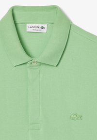 Grön polo skjorta i texturerat tyg med en tre-knapps knäppning. Har en liten broderad logotyp på bröstet och en normal passform.