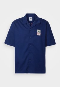 Mörkblå kortärmad skjorta i bomull, med knappar, krage och ett grafiskt märke på vänster sida. Slät textur.