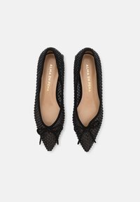 Bailarinas negras de punta afilada con parte superior de malla texturada y detalle de lazo. Plantilla de un beige claro con marca en dorado. Forro interior suave.