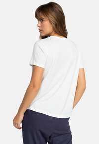 Camiseta de algodón blanca con mangas cortas enrolladas y cuello redondo, con una textura suave y un corte holgado, combinada con pantalones azul marino.