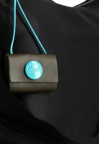Bolso de cuero negro con una solapa rectangular verde. Presenta un botón azul con el logo "Gabs" y un cordón de sujeción azul.